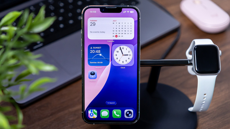 An iPhone on a charging stand with an Apple Watch, showing widgets on its screen.
