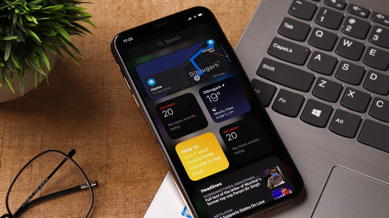 An iPhone on top of a laptop, with several widgets on the screen.