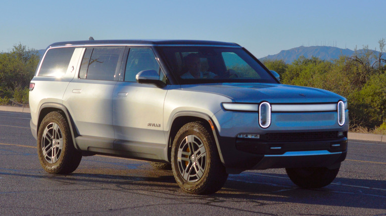 2025 Rivian R1S driving through a rural desert highway.