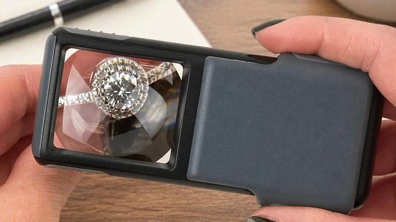 A person holding the Carson MiniBrite LED magnifier to inspect a diamond ring.