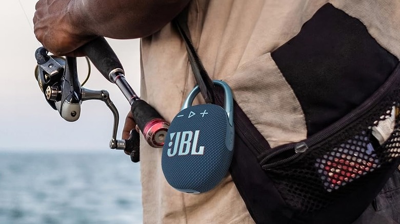 The JBL Clip 5 Bluetooth speaker clipped onto a bag while a person is fishing.