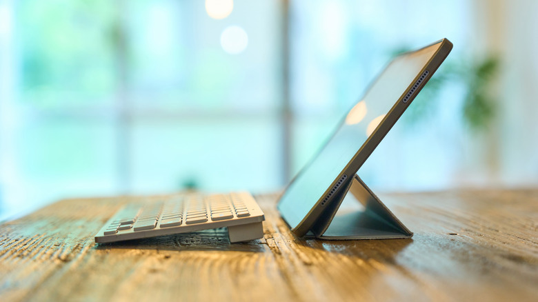 A tablet propped up on a stand, with a keyboard next to it on a wooden table