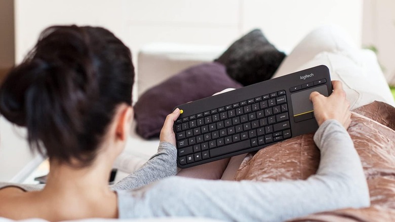 A person holding the Logitech K400 Plus Bluetooth keyboard with two hands on the comfort of their couch