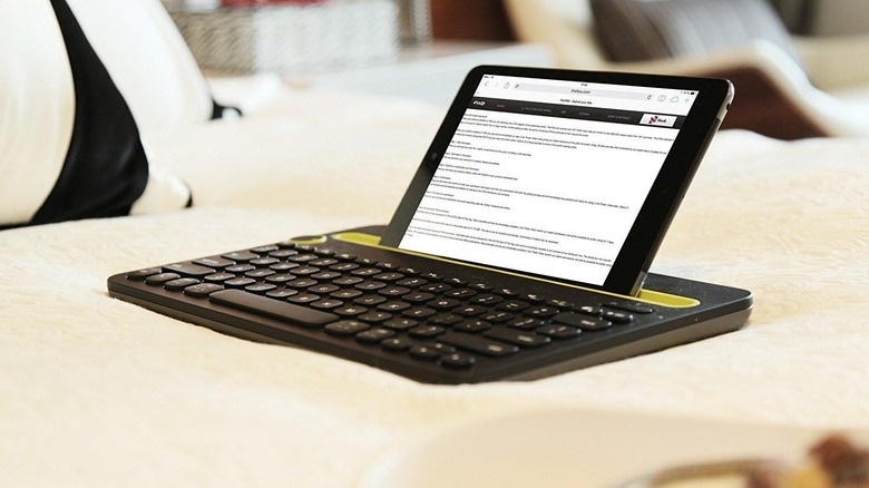 The Logitech K480 keyboard, with a tablet in its cradle, placed on a soft-looking surface