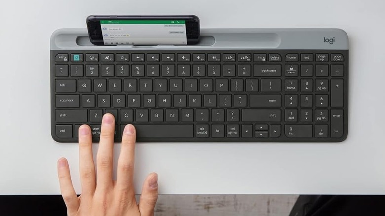 A hand on the Logitech K585 Bluetooth keyboard, with a phone placed in its cradle
