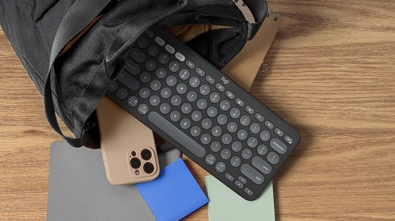 The Logitech Pebble Keys 2 K380s keyboard halfway placed in a bag on a wooden table, along with a phone