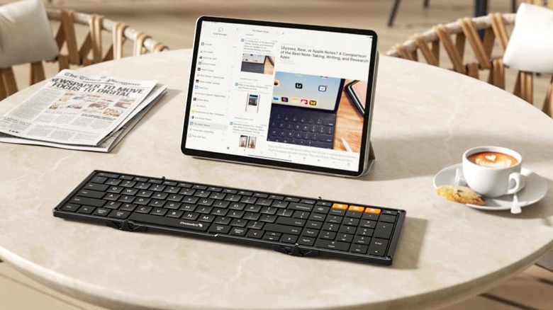 The ProtoArc XK01 Bluetooth keyboard placed on a circular table, with a tablet, cup of coffee, and a newspaper around it