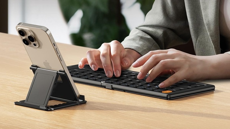 A person using the ProtoArc XK04 Bluetooth keyboard while propping up a mouse on a stand in front of it