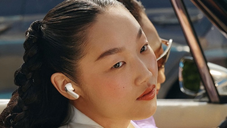 A woman sits in a car while wearing white Samsung buds.