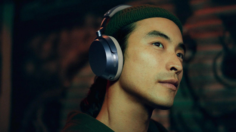 A man in trendy hip-hop style clothing stares off camera while wearing Sennheiser headphones.