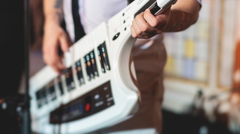 A person playing a white keytar in a home studio setting.