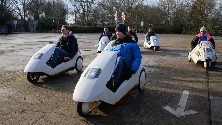 People riding in Sinclair C5s in a parking lot during a group gathering.