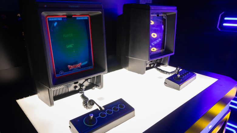 Vectrex home gaming consoles displaying vector-graphics games with wired controllers.