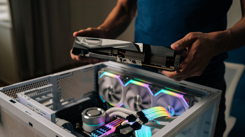 Person installing a graphics card into a custom-built desktop PC with RGB lighting.
