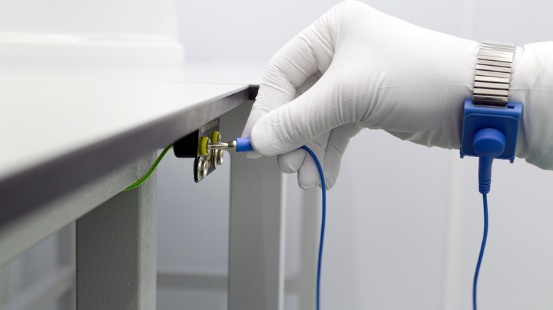 A white gloved hand connecting an anti-static wrist strap to a ground source.