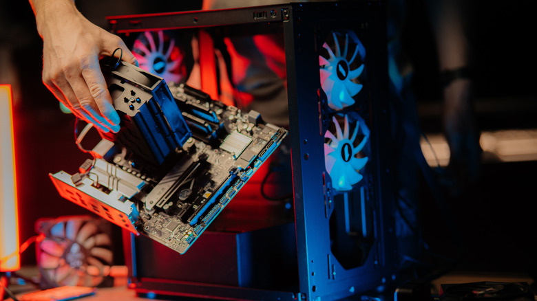 A person installing a motherboard with a large CPU cooler into a desktop PC case.