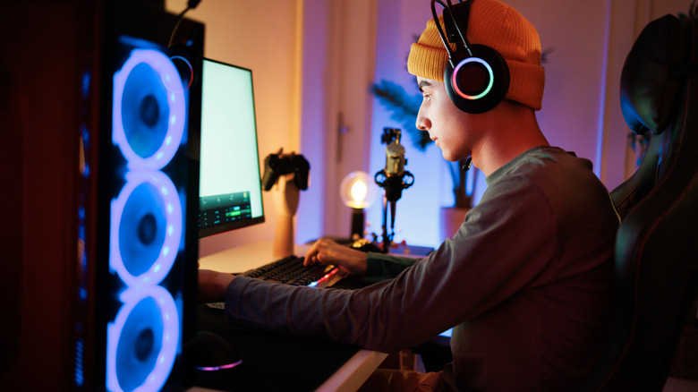 A person wearing over-ear headphones using a desktop gaming PC with RGB-lit cooling fans.