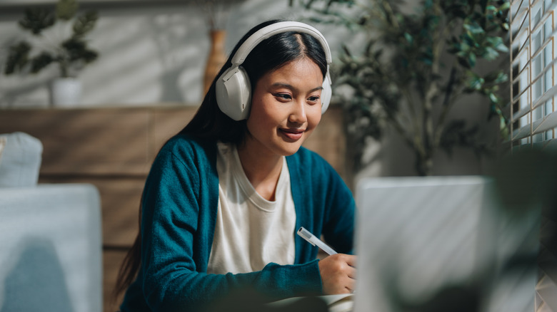 A student taking notes while watching a video on her laptop with headphones on