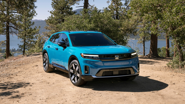 An electric blue Honda Prologue parked on a dirt clearing surrounded by trees