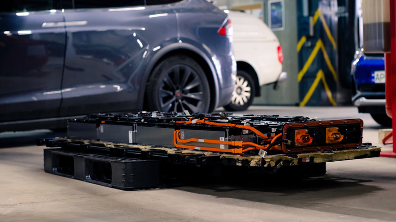 A battery pack next to a parked EV in a workshop.