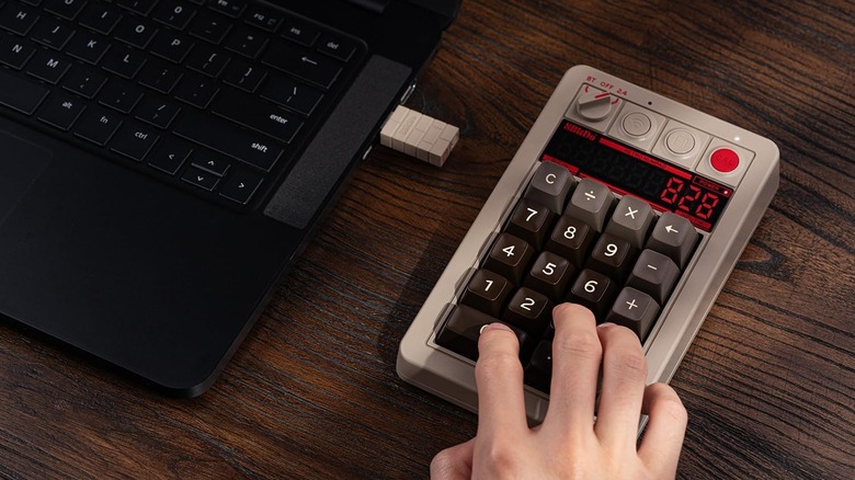 A person typing on a retro wireless numpad next to a laptop with a dongle plugged in.