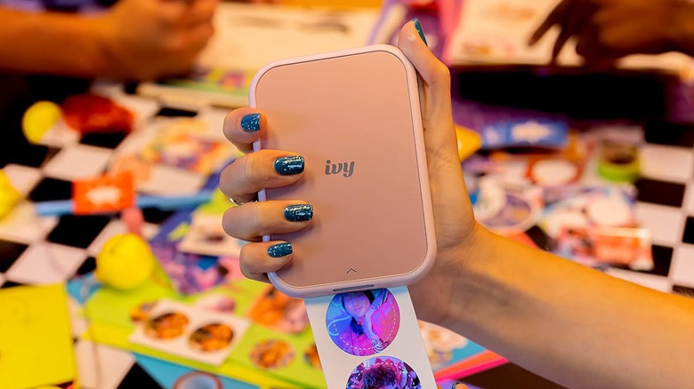 A hand holding an Canon Ivy 2 Mini Photo Printer as it prints out stickers.
