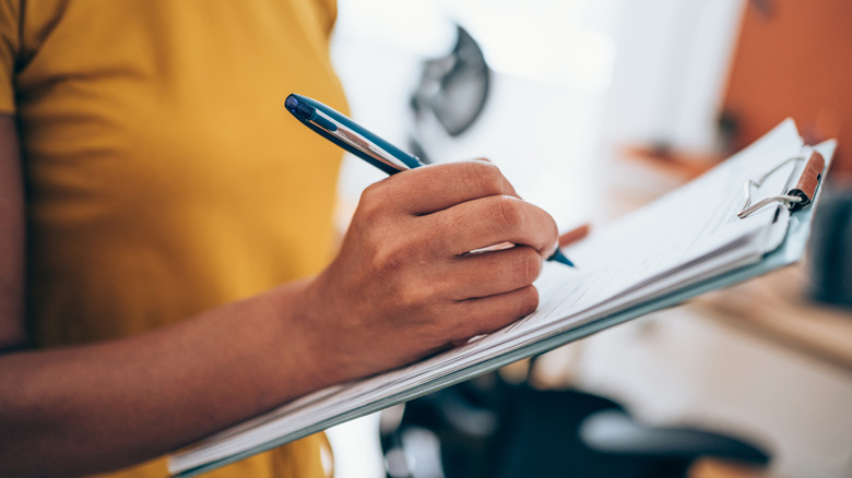 A person writing on a clipboard using a pen.