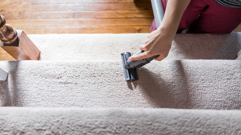Close up view of a person vacuuming the stairs with a small vacuum head