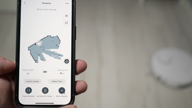 A person holding a smartphone showing progress as the roboto vacuum maps the floor