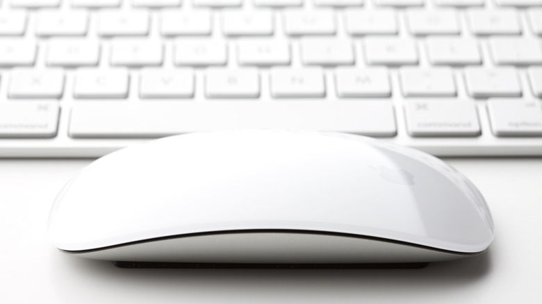 A white Magic Mouse sits on a white table in front of a white keyboard.