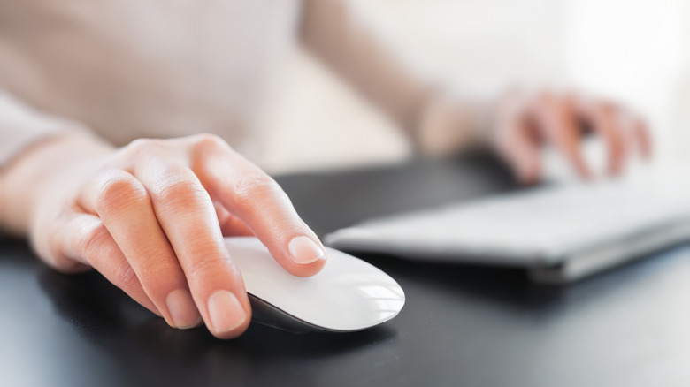 Close-up on the hands of a person sitting at a black desk, using a Magic Mouse and keyboard.