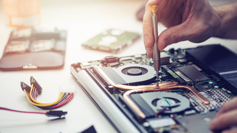 A person repairing the something on the inside of a laptop computer.