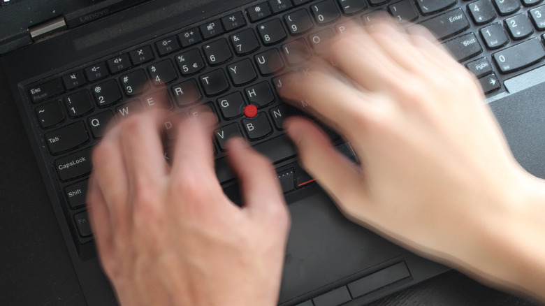 A pair of hands blur as they type on a ThinkPad keyboard.