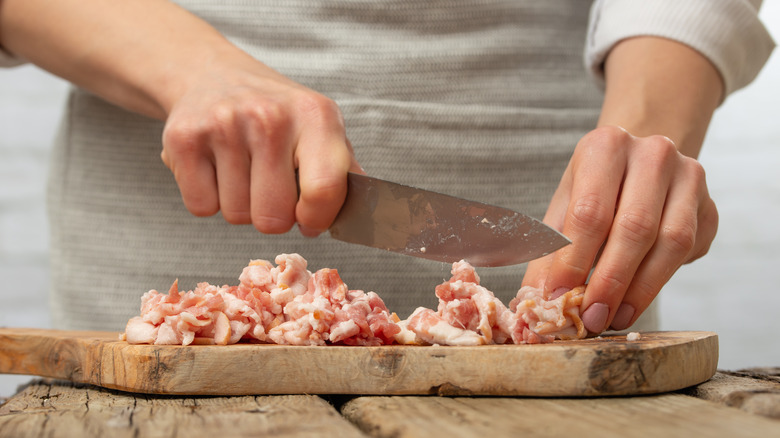 Person cutting bacon on a wooden chopping board