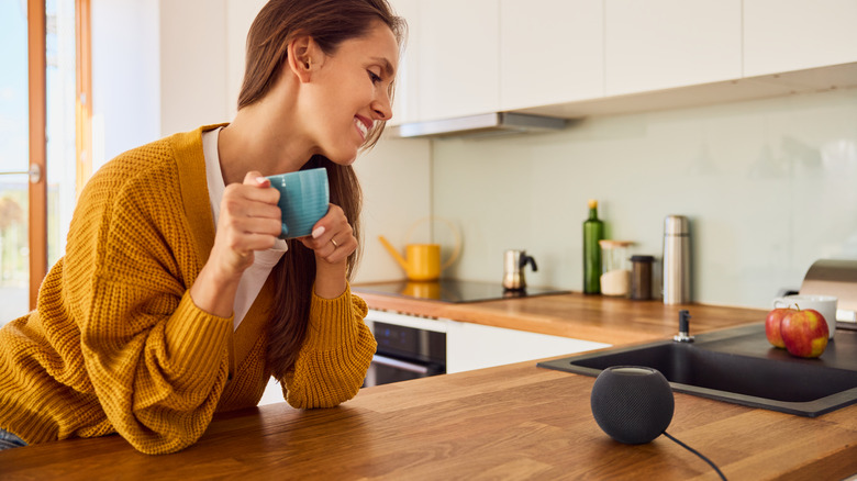 Young woman drinking coffee while conversing with a smart speaker