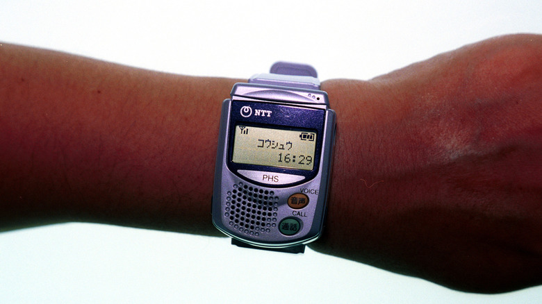 A PHS phone wristwatch on a person's arm shows the time.