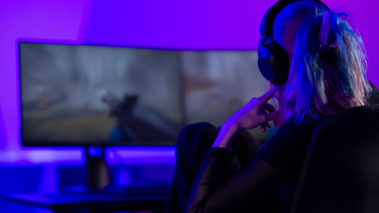A woman plays video games on a dual-monitor gaming system.