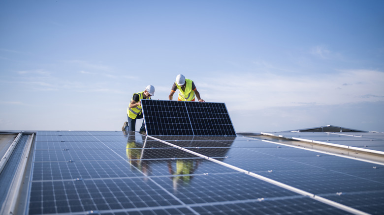 Two workers install a solar panel on a roof.