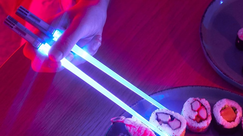 A hand using the ChopSabers to pick up sushi