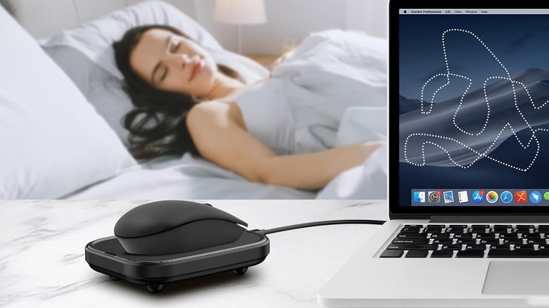 The Yonktoo Mouse Jiggler connected to a Macbook as a person sleeps in the background on a bed