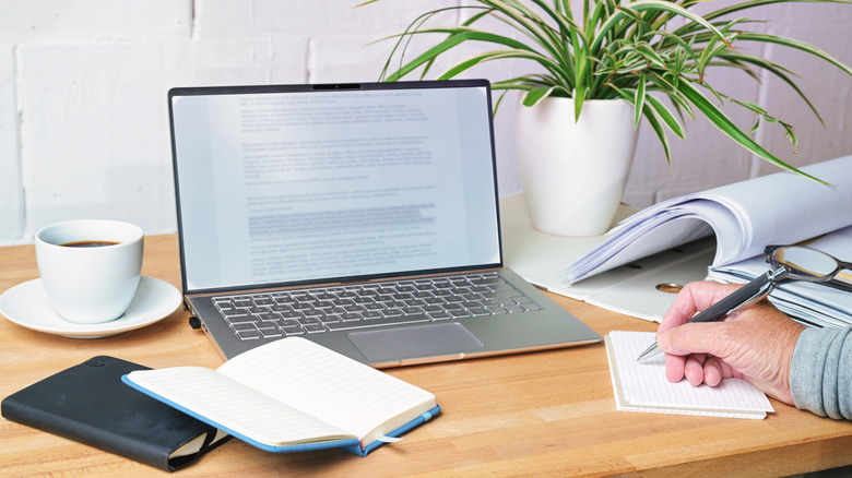 Text selected on a word document open on a laptop, placed on a desk where a person is taking notes