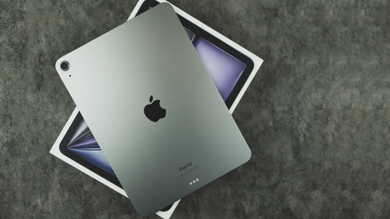 An iPad Air, on top of its retail box on a gray surface.