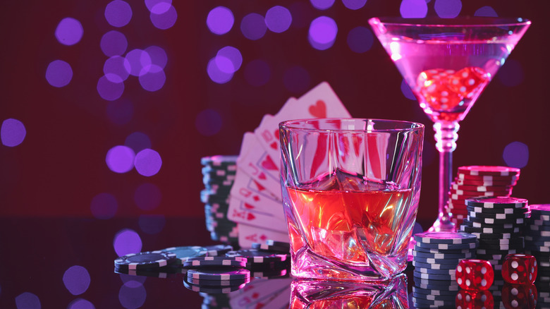 Two cocktails sit on a table next to dice, cards, and poker chips.