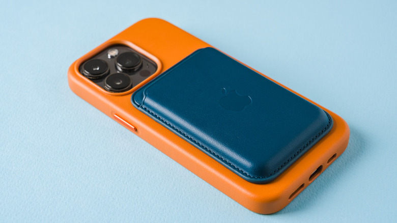 An Apple MagSafe wallet attached to the back of an iPhone in an orange case