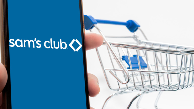 The Sam's Club logo on a phone, with a mini shopping cart beside it.