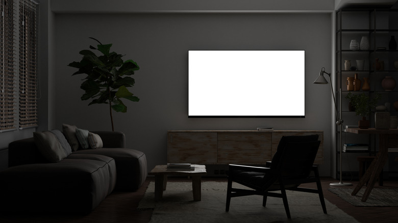 Glowing TV screen mock up at night in the living room with white wall.