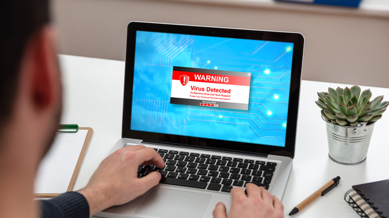 A person looking at a laptop with the words Virus Detected on the screen.
