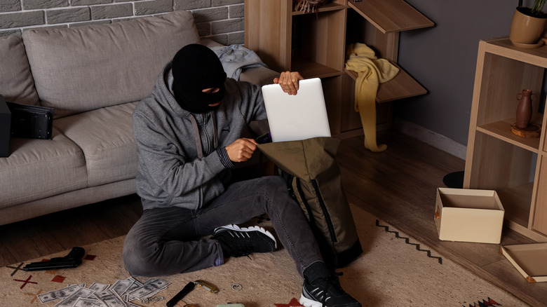 A masked thief slipping a stolen laptop into a bag.