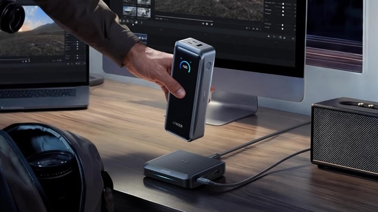 A hand placing an Anker Prime 26K, 300W power bank on its charging case.