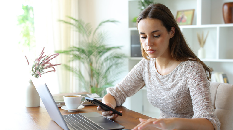 A woman using multiple connected devices on a wooden table in a home setting.